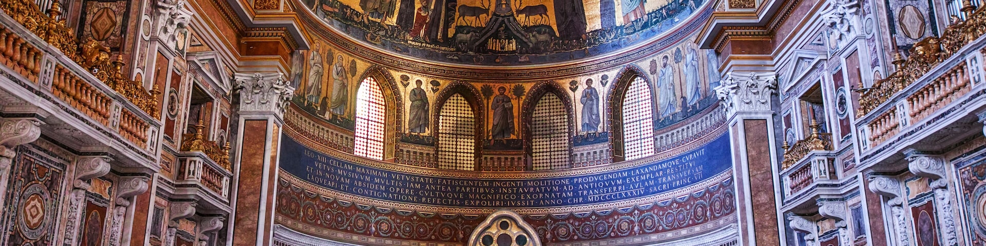 Interior de igreja ornamentado, com afrescos detalhados, uma cúpula central e uma cruz imponente.