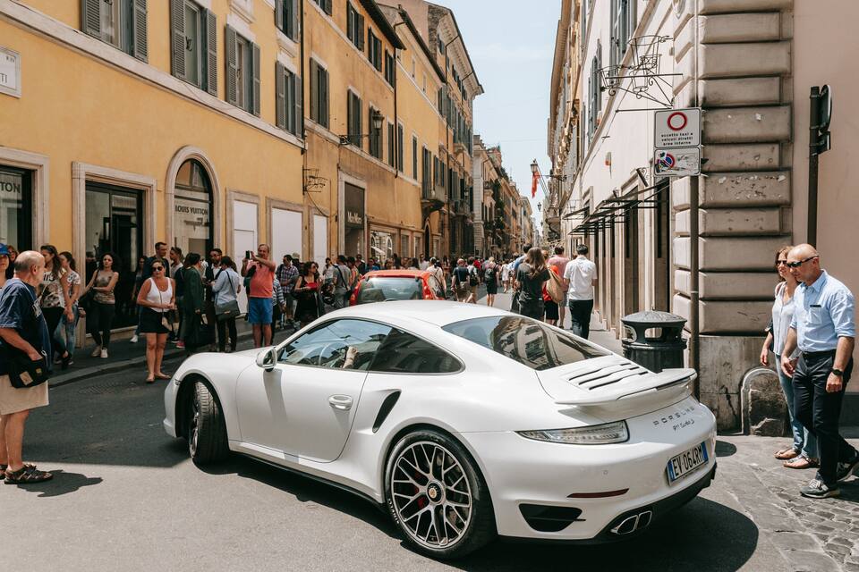 A white Porsche parked on a cobblestone street lined with historic buildings and storefronts.