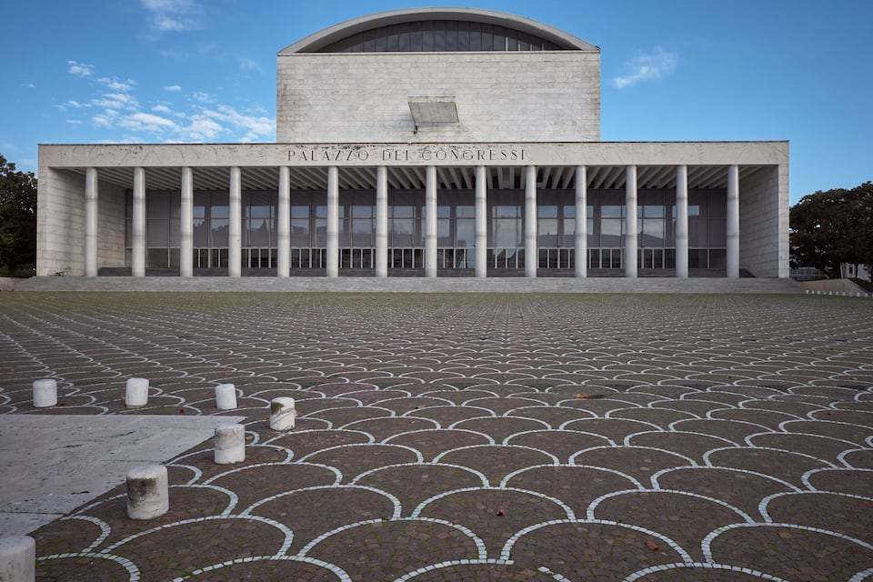 The exterior of the Palazzo del Parlamento building with a large open plaza in front.