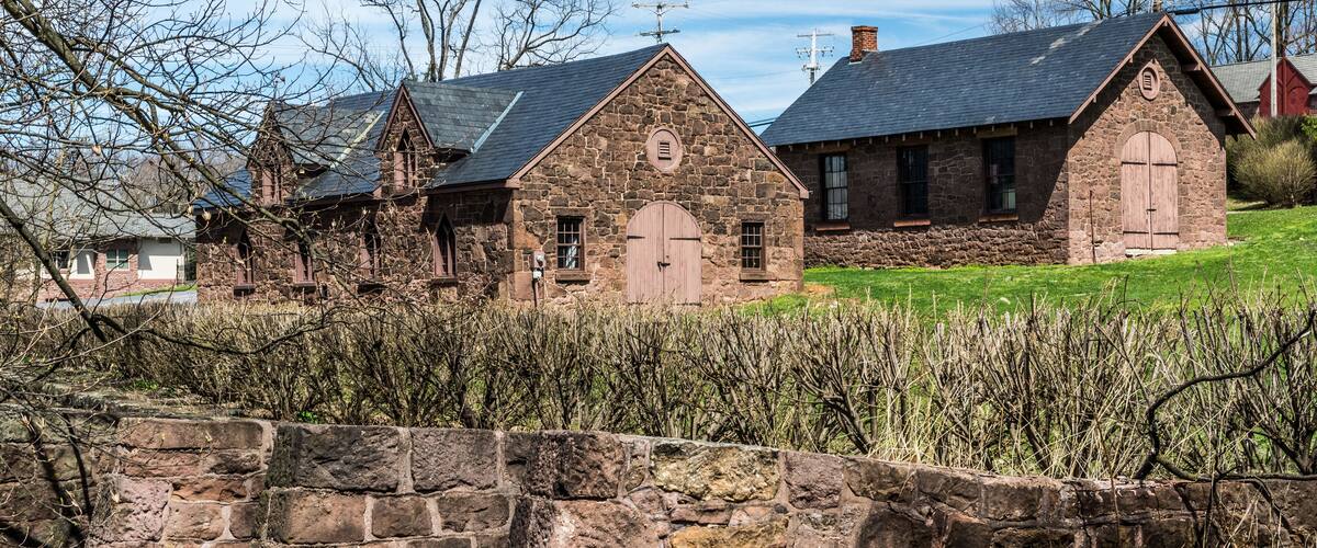 A stone building with a large wooden door, surrounded by a stone wall and vegetation.