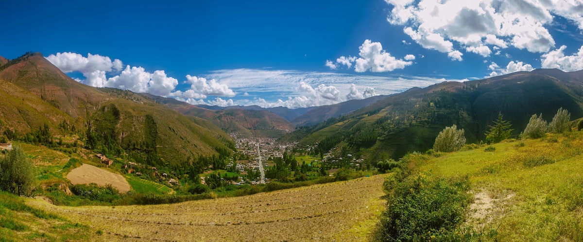 A valley with terraced fields, a distant town, and mountains under a clear sky.