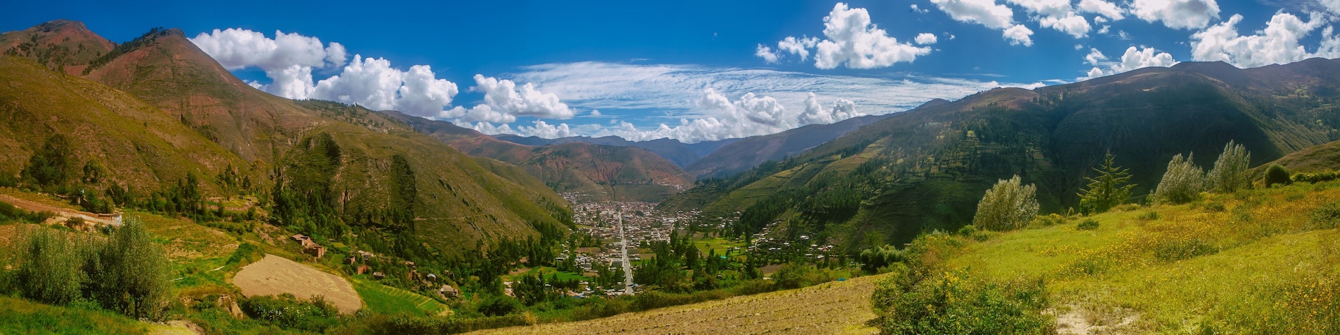 A valley with terraced fields, a distant town, and mountains under a clear sky.