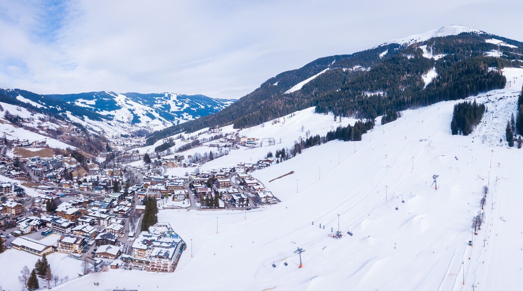 Aerial view of the mountain ski resort village in Austrian Alps with large mountain slopes, skiers, snowboarders, ski lifts and small winter town.