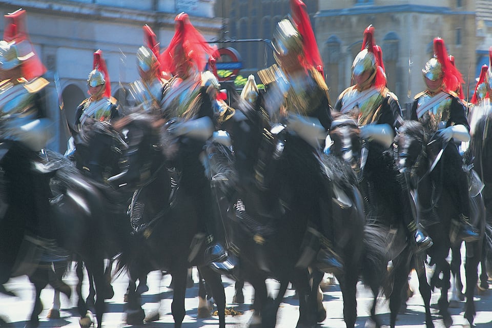 A group of mounted guards in historical armor, riding horses in a parade.