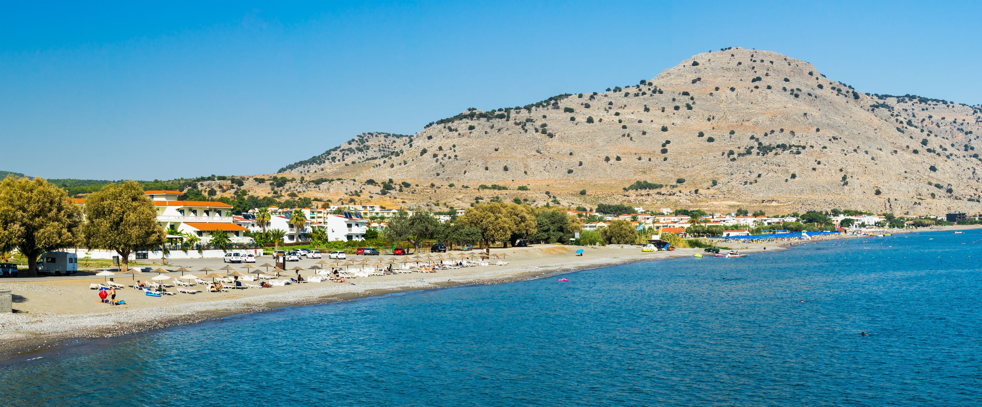 A coastal town with a beach, a mountain in the background, and a clear blue sky.