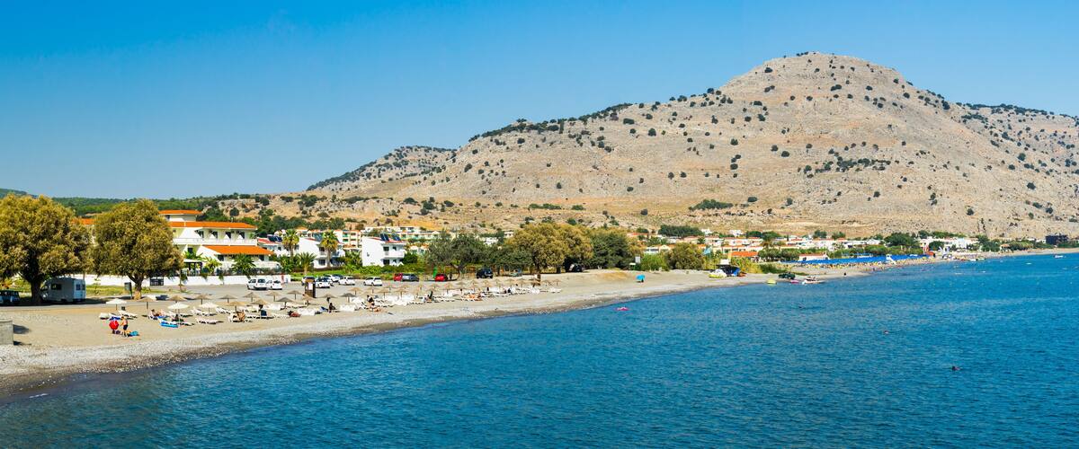 A coastal town with a beach, a mountain in the background, and a clear blue sky.