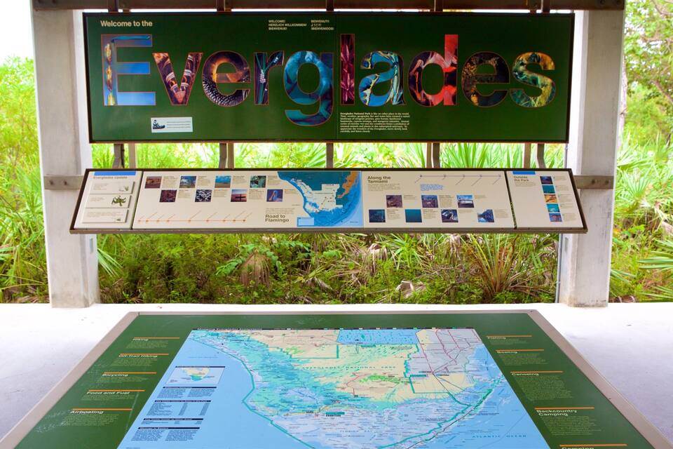 Un cartel con la palabra 'Everglades' escrita en letras de colores, un mapa debajo y follaje circundante.