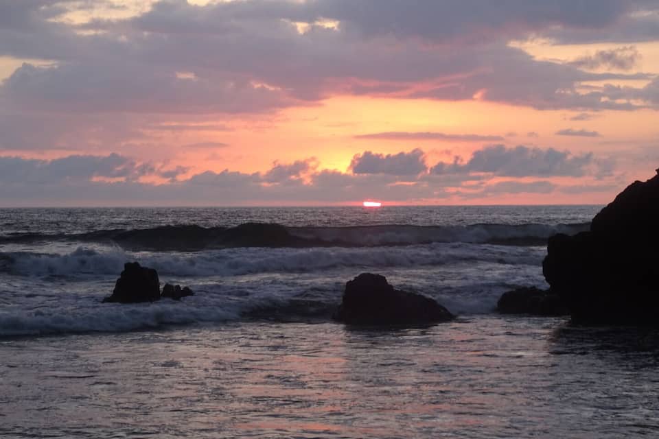A sunset over the ocean with waves crashing against rocks.