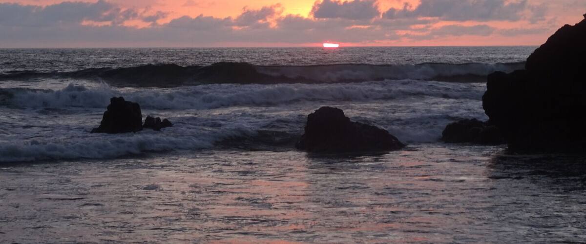 A sunset over the ocean with waves crashing against rocks.