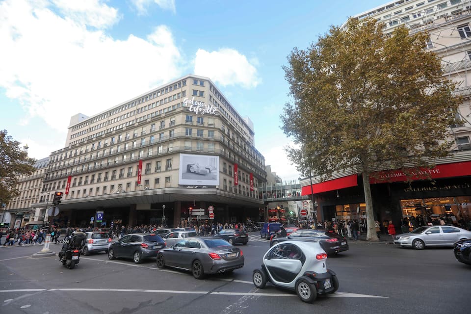 Una concurrida intersección urbana con un edificio grande que muestra un cartel publicitario llamativo.