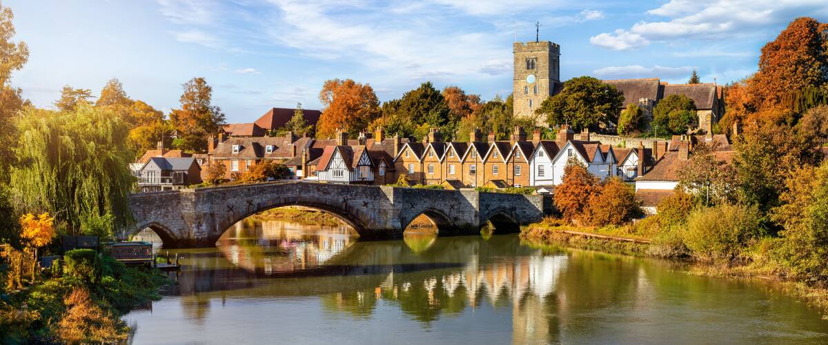 A stone bridge over a river, surrounded by autumn-colored trees and historic buildings.