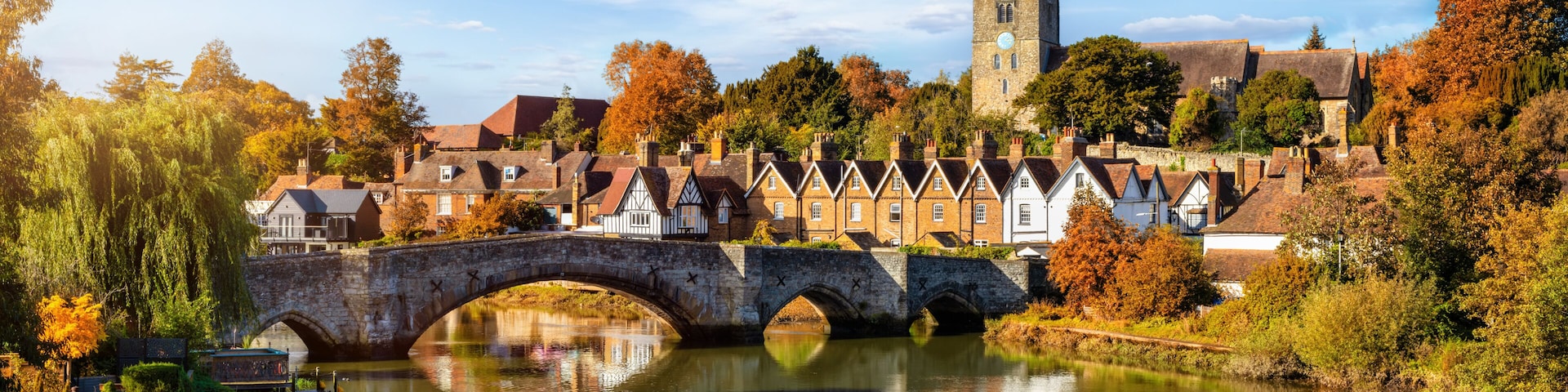 A stone bridge over a river, surrounded by autumn-colored trees and historic buildings.