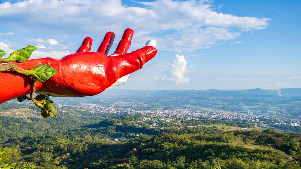A red hand sculpture with a view of a town and mountains in the background.