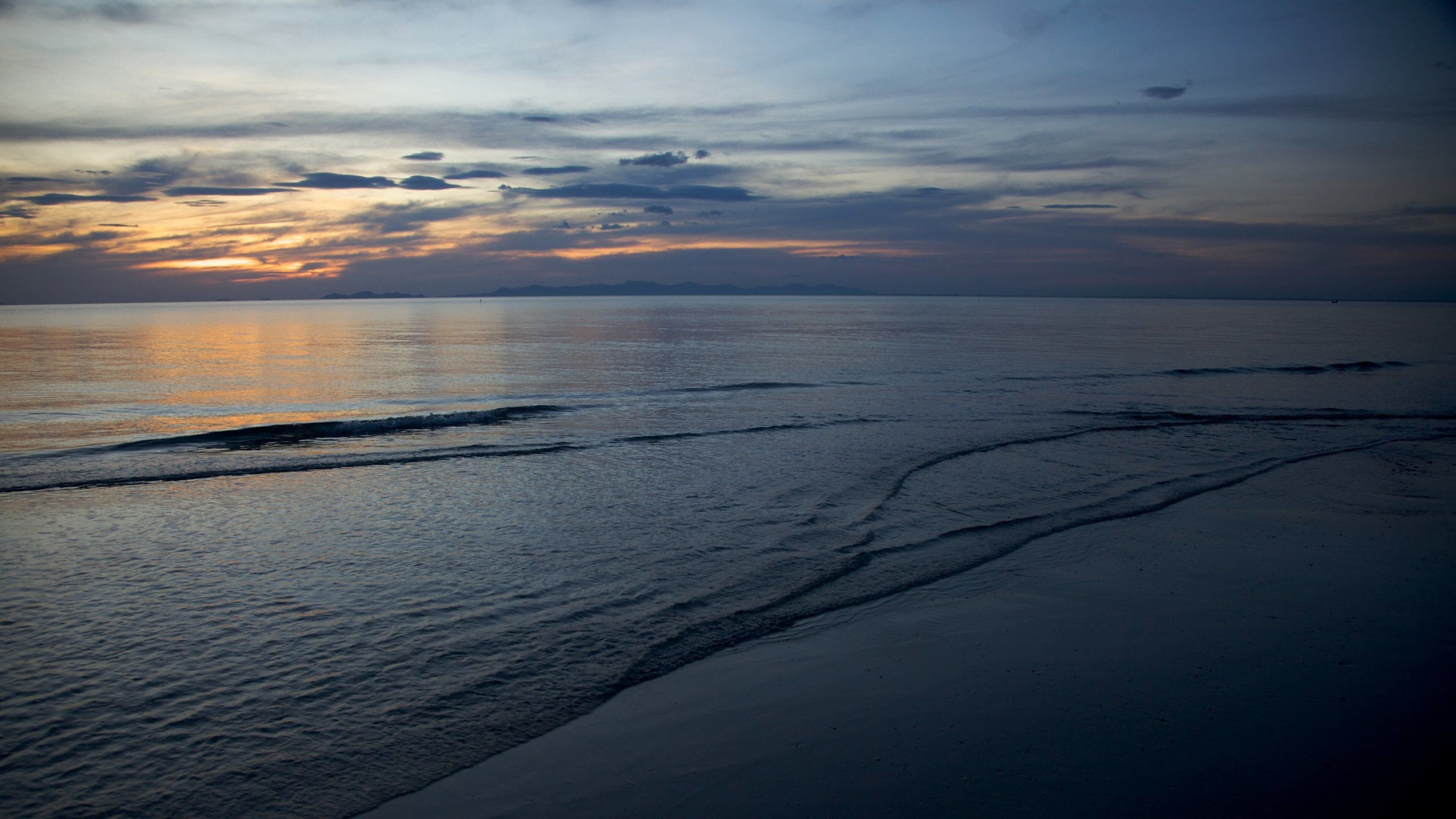 A beach with gentle waves and a sunset sky.