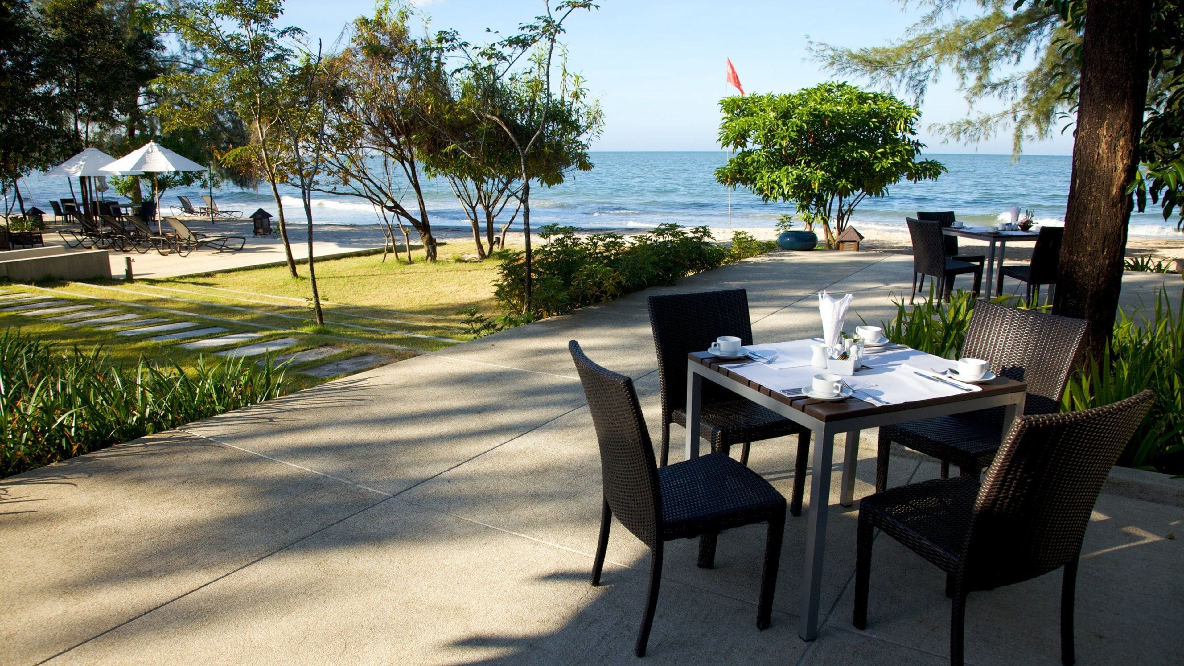 A seaside restaurant with outdoor seating, a view of the ocean, and a flag in the background.