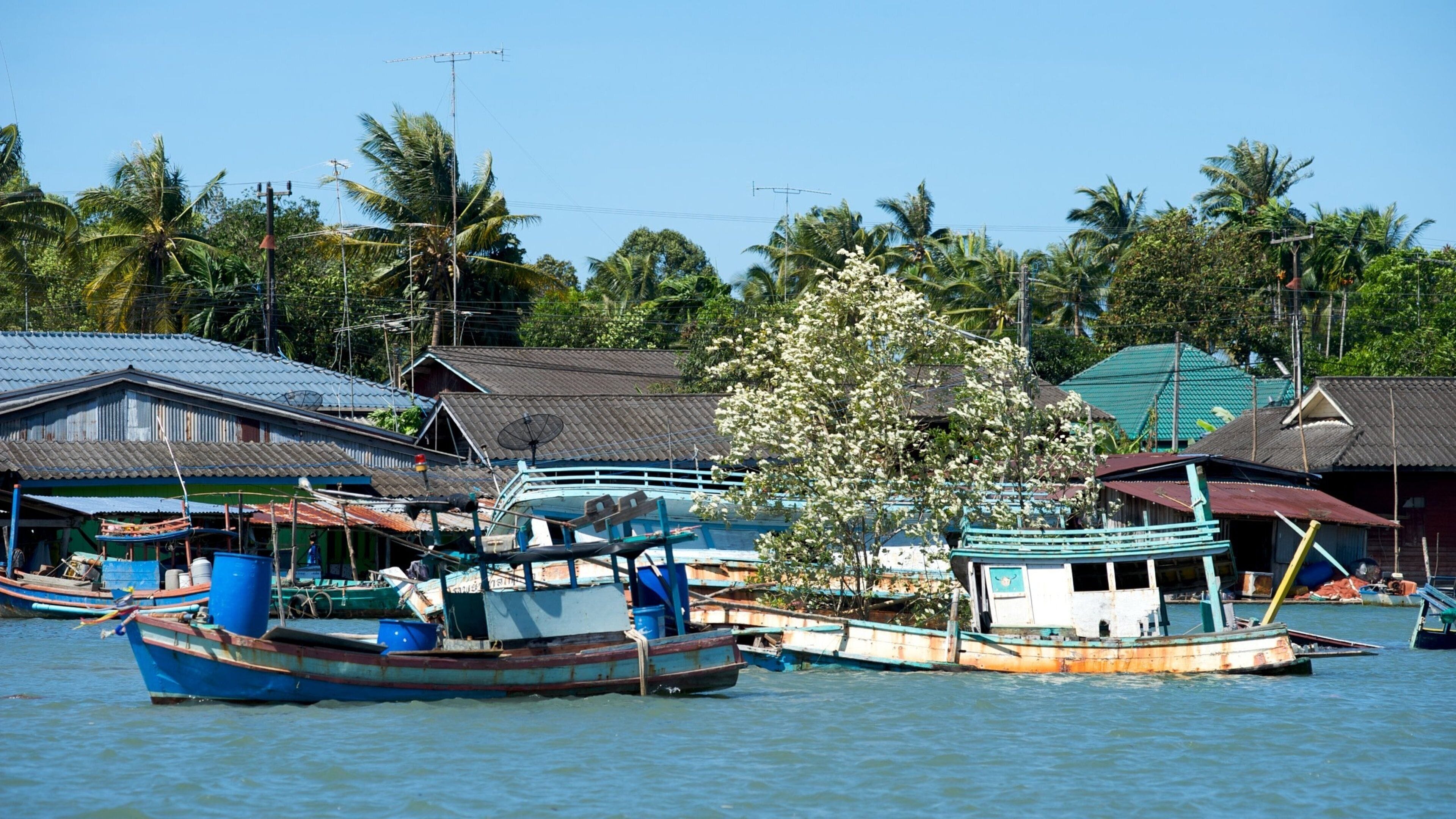 A waterway with several boats docked, surrounded by traditional houses with metal roofs and palm trees.