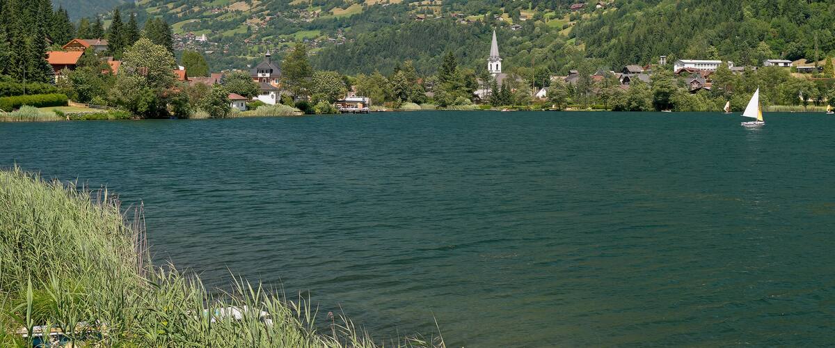 A lake with a sailboat, surrounded by houses, a church, and a mountain.