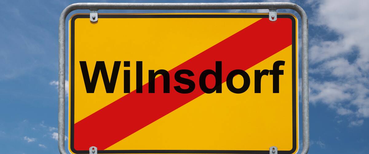 A road sign with the text "Wilnsdorf" against a blue sky with clouds.