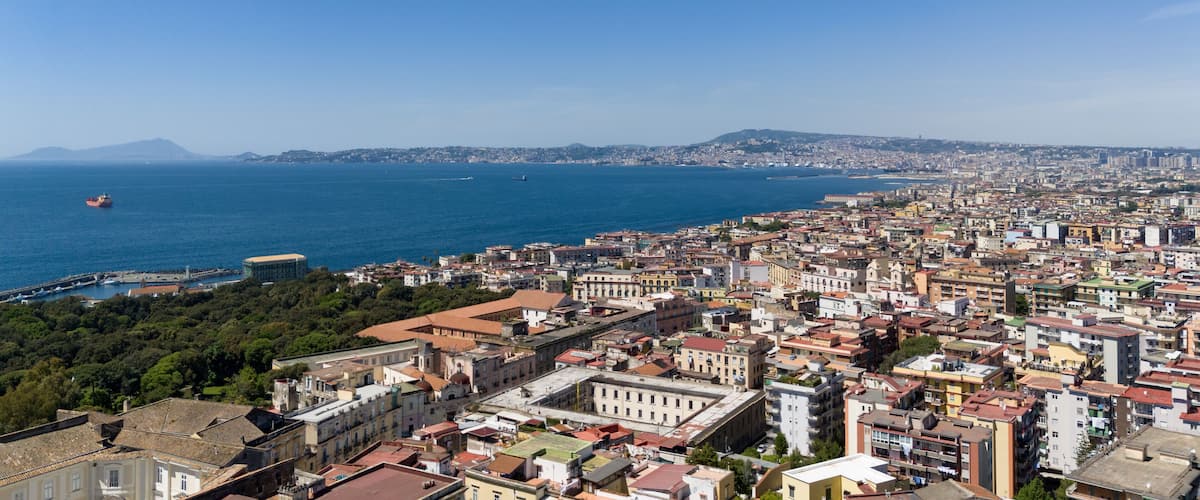 A coastal cityscape with a view of the sea, a ship, and a distant mountain.