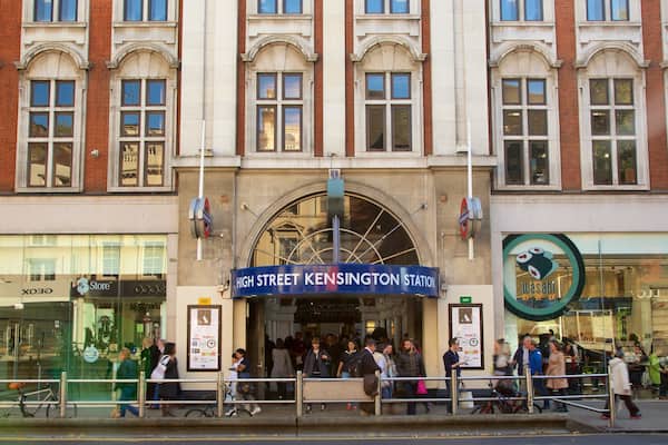 Eine belebte Straße mit einem gut sichtbaren Schild der High Street Kensington Station, einem Laden mit Glasfassade und einem Sushi-Restaurant.