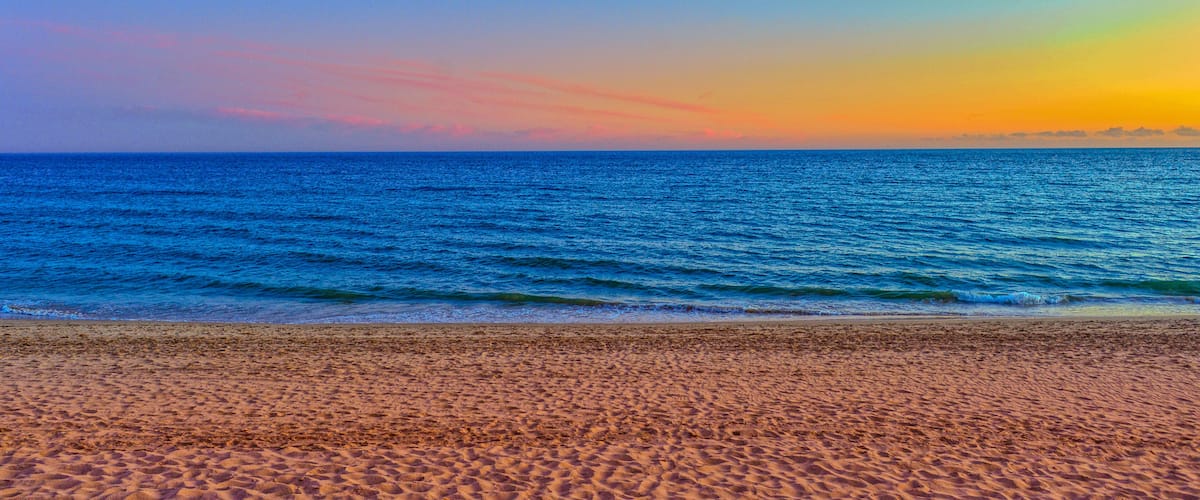 A beach with sand and ocean waves during sunset.