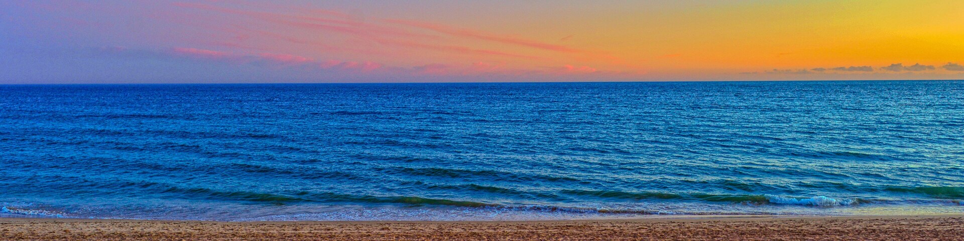 A beach with sand and ocean waves during sunset.