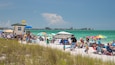 A crowded beach with people sunbathing and swimming, colorful umbrellas, and a lifeguard tower.