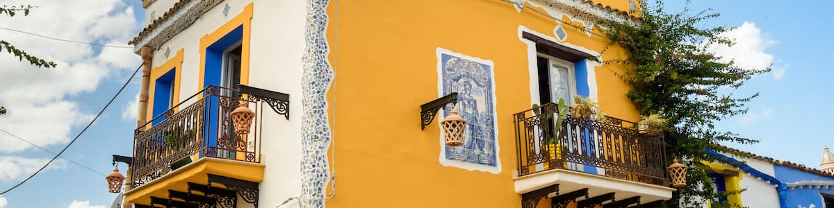 A yellow building with blue accents, a balcony with a lantern, and a pineapple decoration on the roof.
