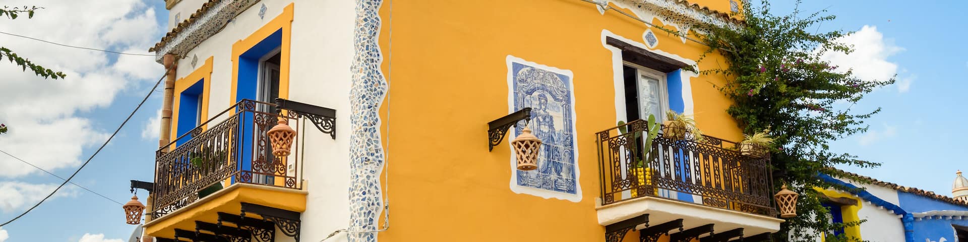 A yellow building with blue accents, a balcony with a lantern, and a pineapple decoration on the roof.