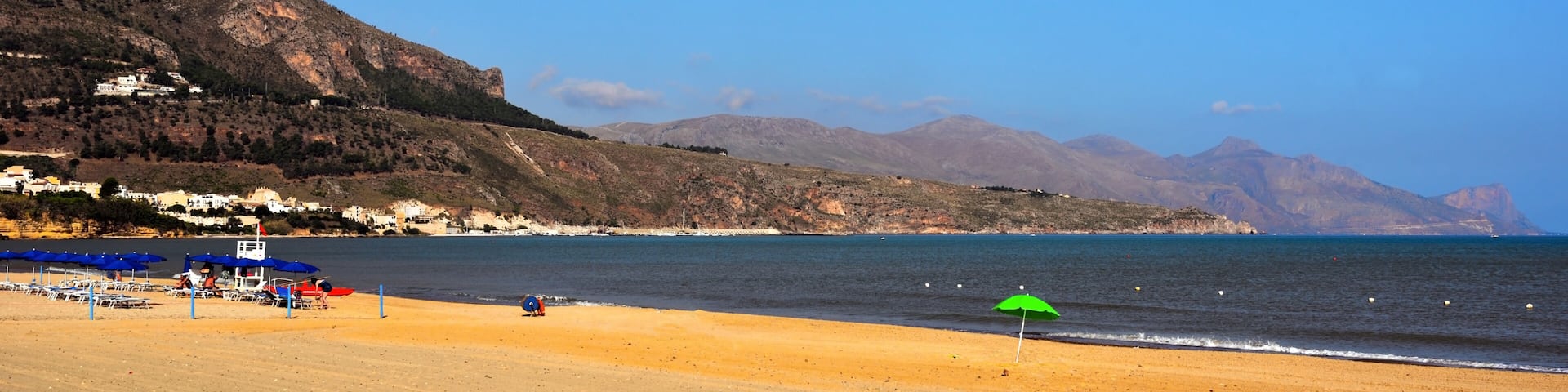 A beach with a green umbrella, a clear sky, and mountains in the background.