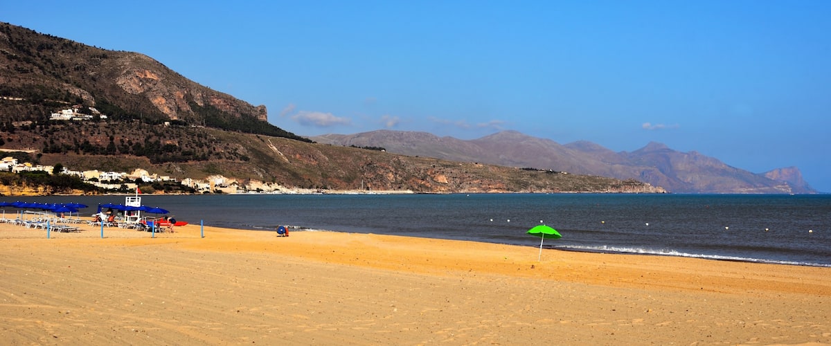 A beach with a green umbrella, a clear sky, and mountains in the background.