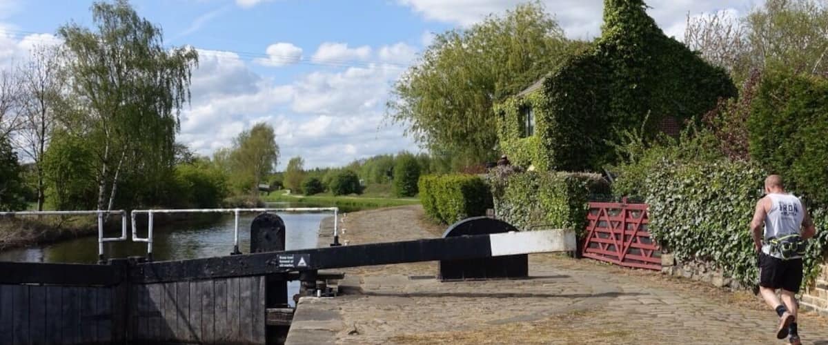 A canal with a lock gate, a stone pathway, and a person running.