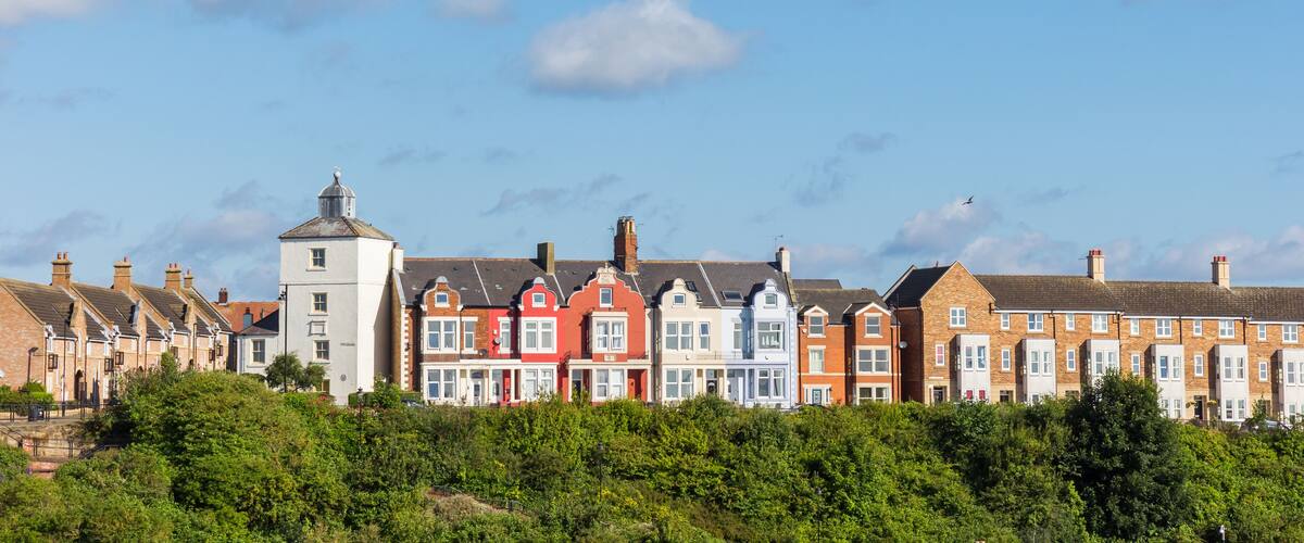 A row of colorful terraced houses with a tower and lush greenery in the foreground.