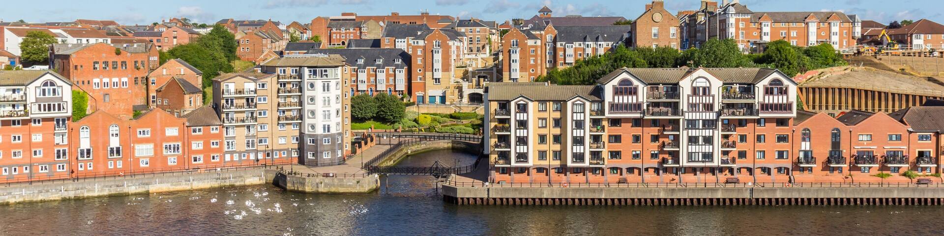 A riverside town with red brick buildings, a bridge, and a clear blue sky.