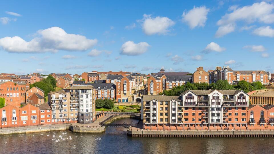 A riverside town with red brick buildings, a bridge, and a clear blue sky.