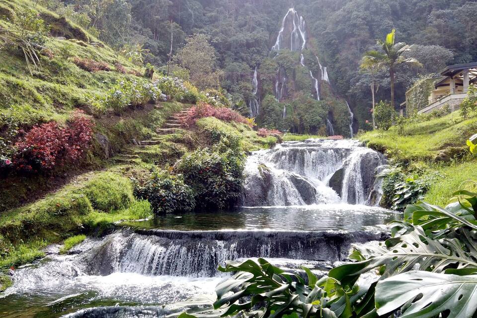 Una cascata impetuosa circondata da una vegetazione rigogliosa e un piccolo edificio.