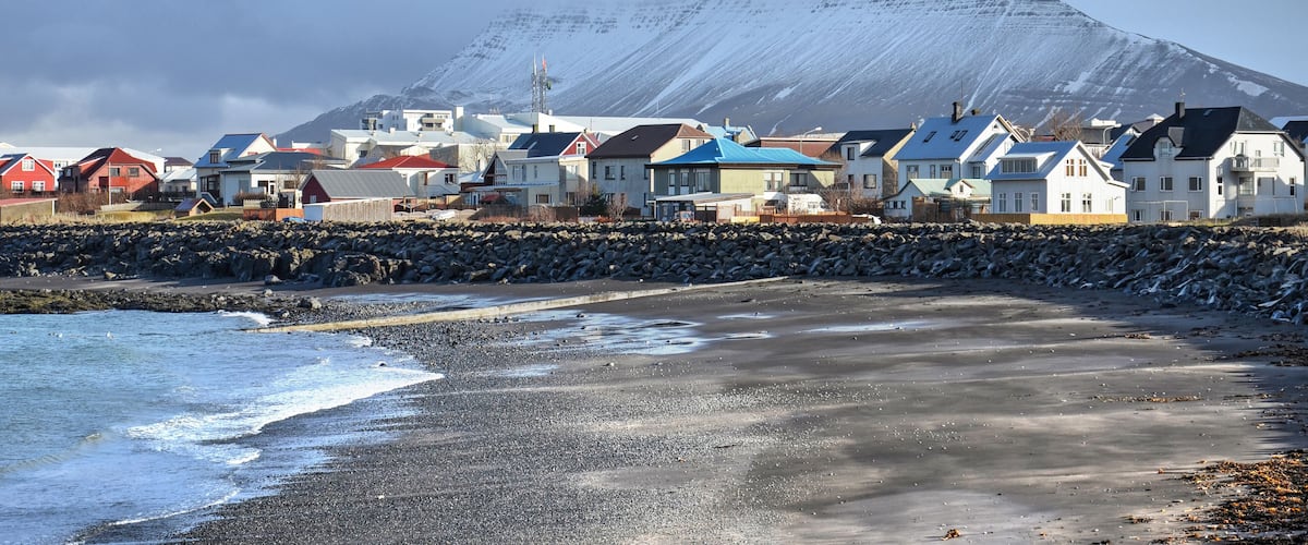 A coastal town with houses, a rocky shoreline, and a mountain in the background.
