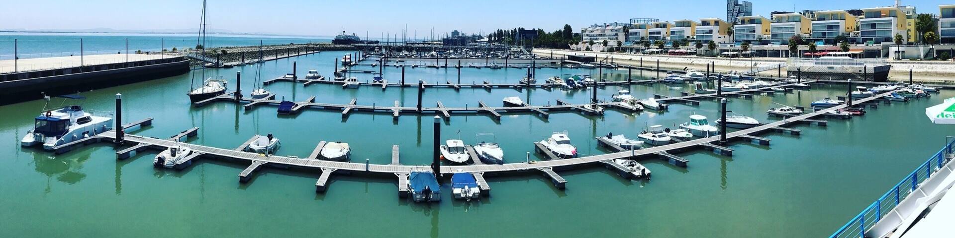 Un puerto deportivo con barcos amarrados, cielo azul despejado y edificios al fondo.