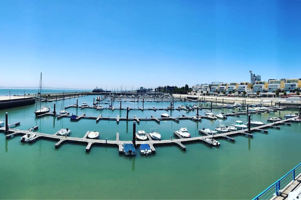 A marina with boats docked, a clear blue sky, and buildings in the background.