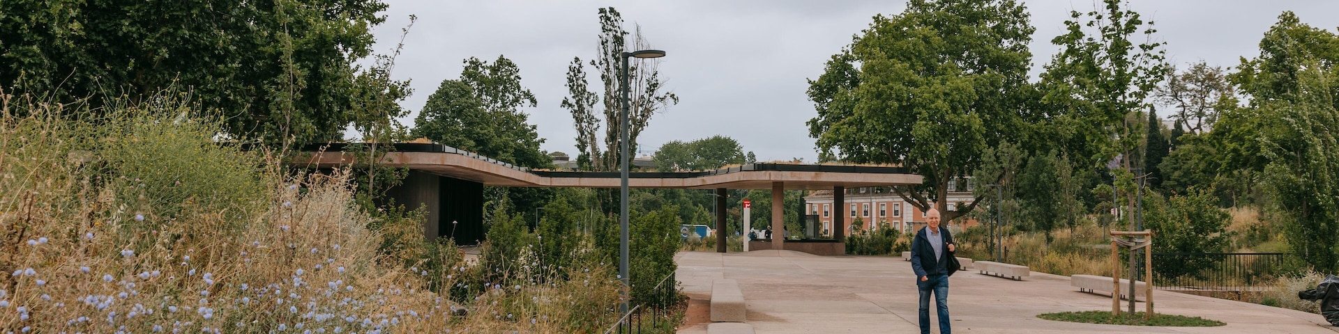 Um parque com um pavilhão coberto, caminhos para pedestres e uma pessoa caminhando.