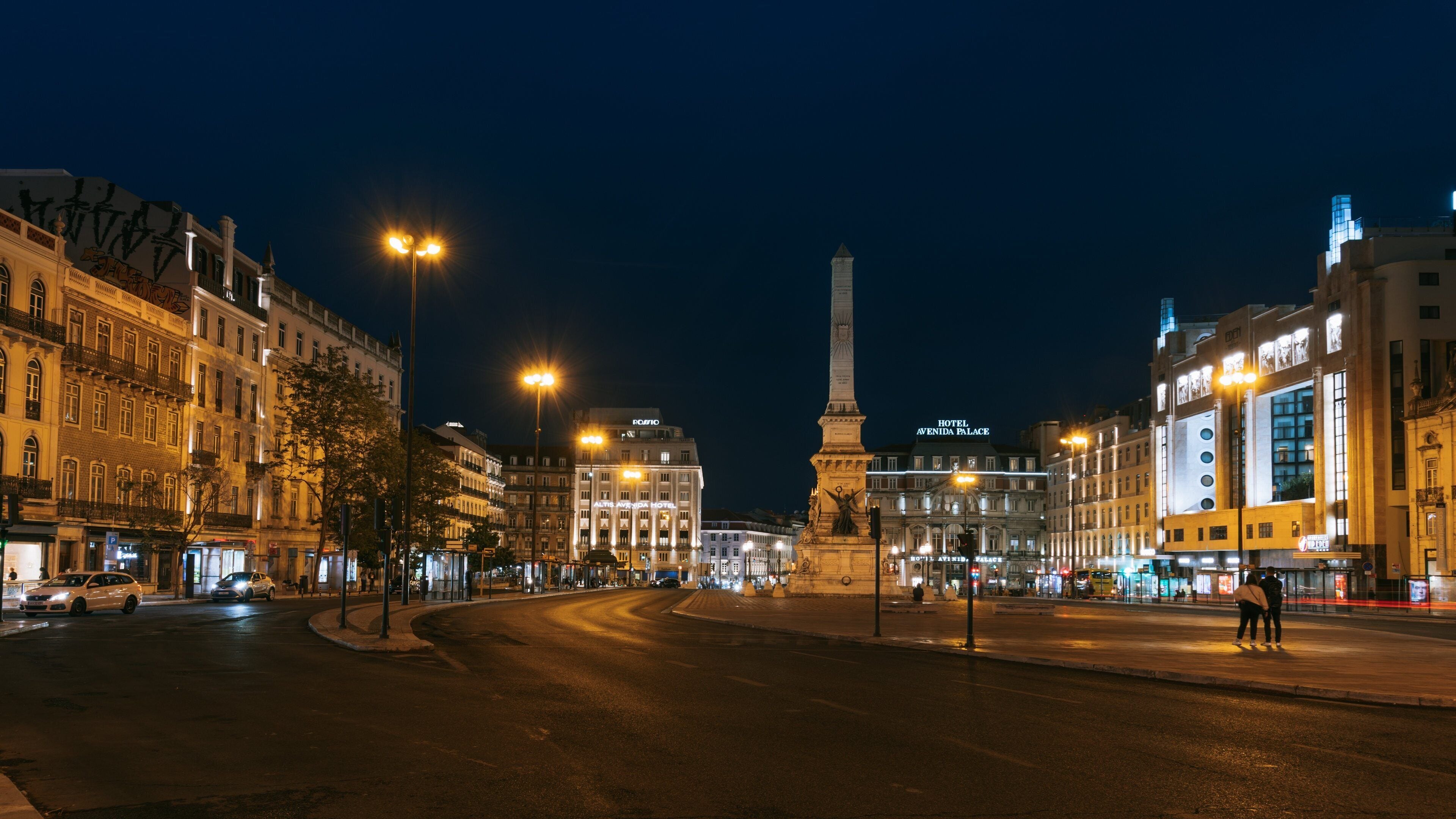 Paesaggio urbano notturno con edifici illuminati, un monumento importante e una rotonda.