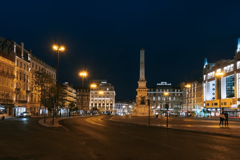 Paesaggio urbano notturno con edifici illuminati, un monumento importante e una rotonda.
