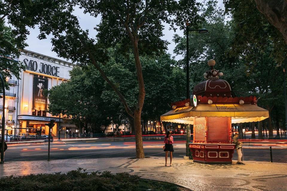 Ein Stadtplatz mit einem Brunnen, Bäumen und einem Gebäude, das 'SAO JOSE' ausweist.