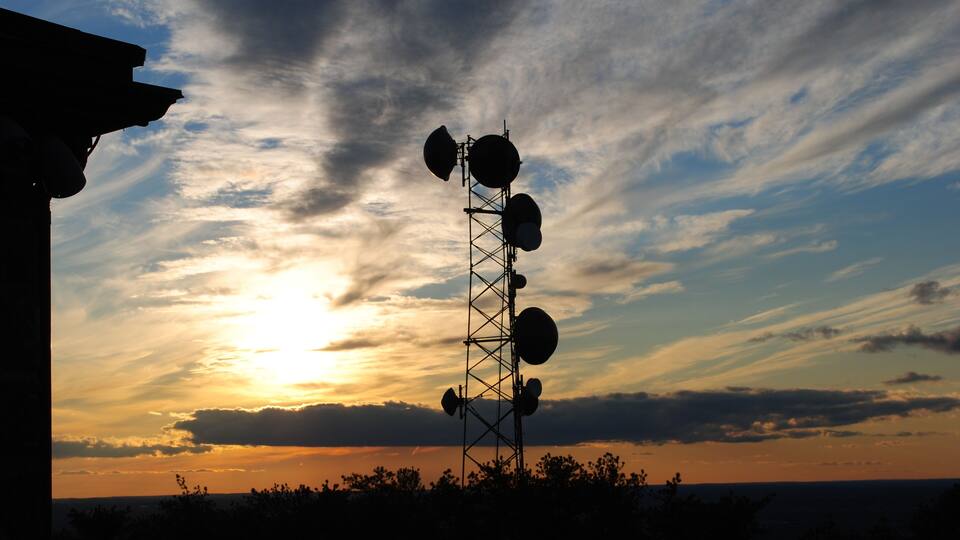 A telecommunications tower silhouetted against a sunset sky.