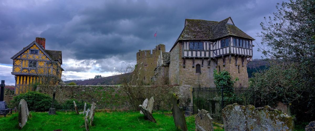 A historic castle with a yellow tower and a stone building with a flag.