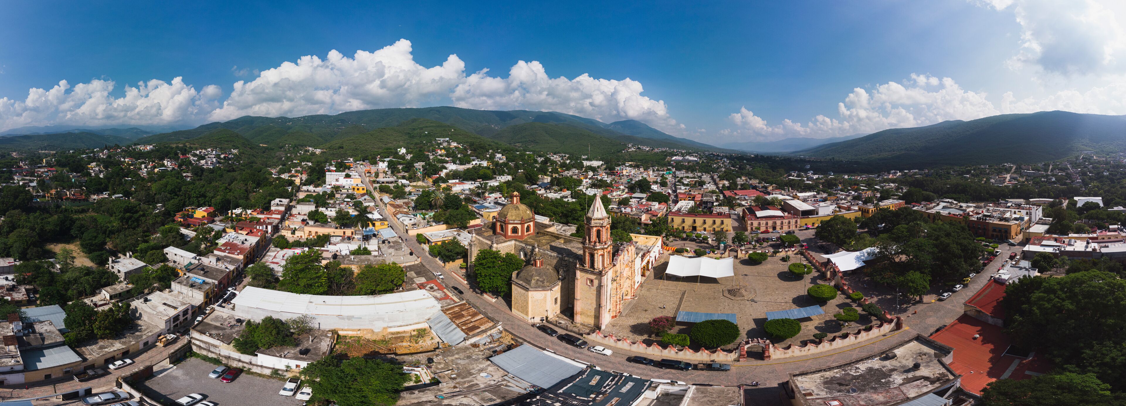 A panoramic view of a town with a prominent church, lush green hills, and a clear blue sky.