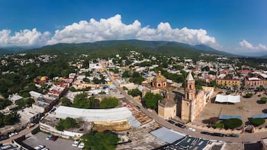 Vista panorámica de un pueblo con una iglesia destacada, colinas verdes exuberantes y un cielo azul despejado.