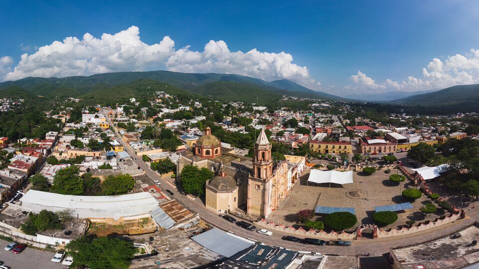 A panoramic view of a town with a prominent church, lush green hills, and a clear blue sky.