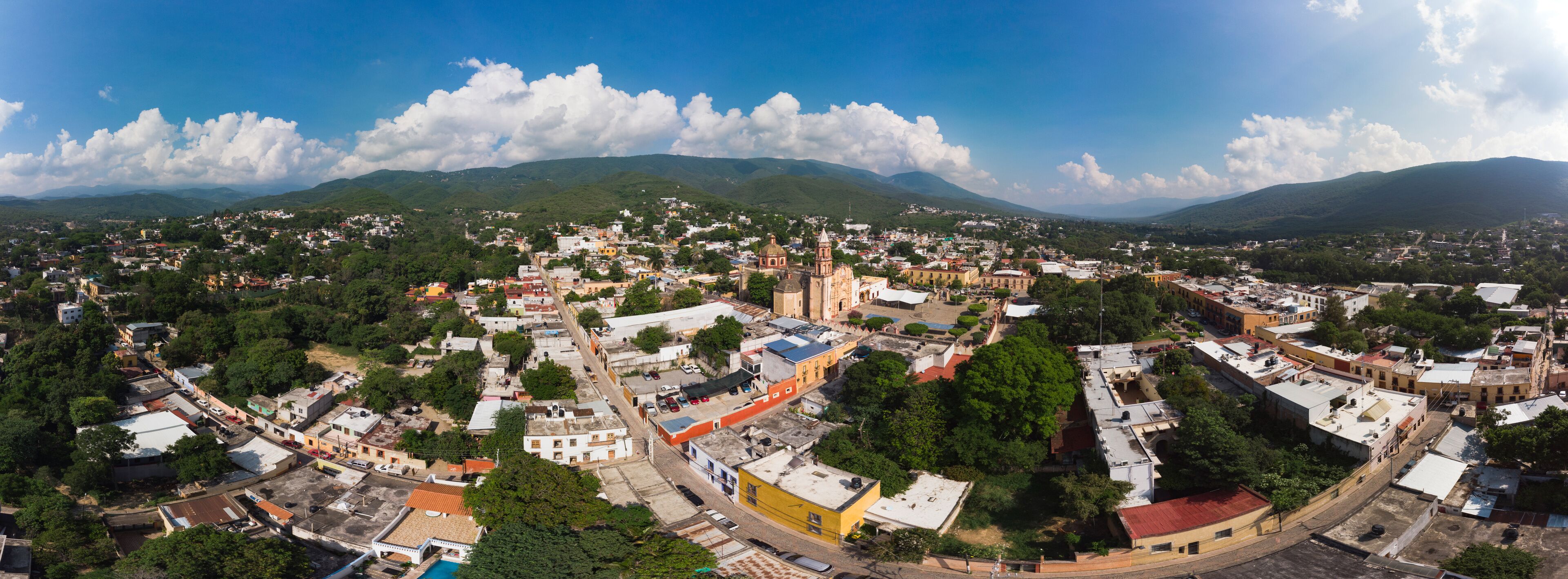 A panoramic view of a town with a prominent church, surrounded by lush green hills and a clear blue sky.