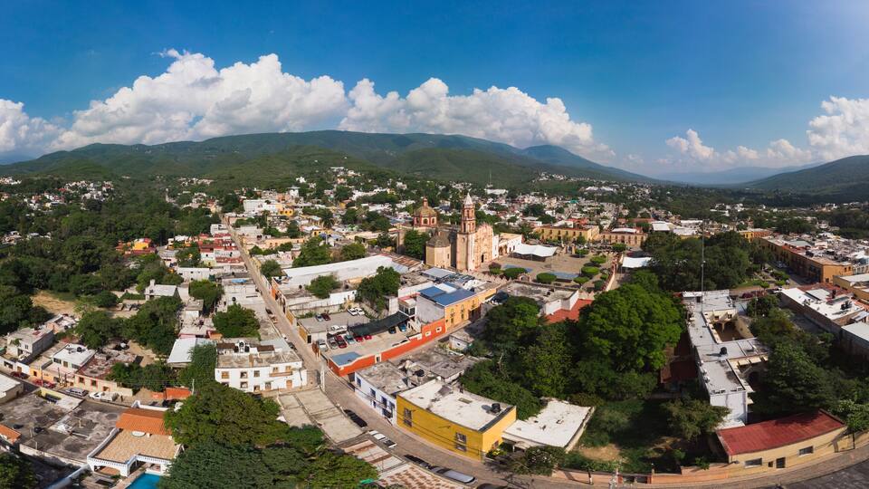 A panoramic view of a town with a prominent church, surrounded by lush green hills and a clear blue sky.